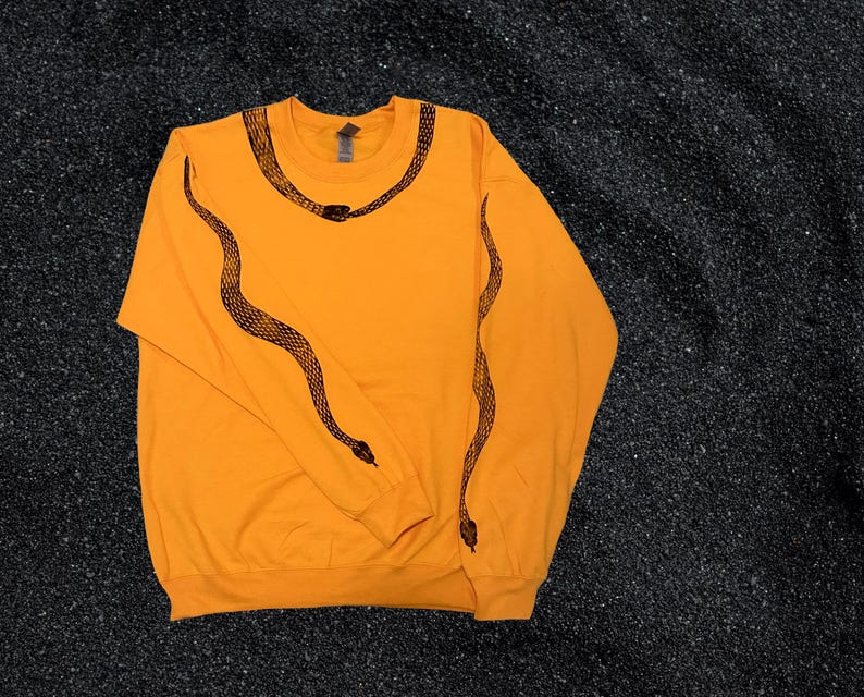 Op de afbeelding: Een feloranje longsleeve sweatshirt met een zwart slangendesign op de mouwen en de halslijn.