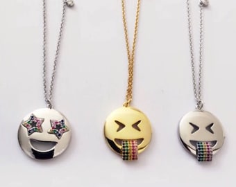 May include: Three silver necklaces with different emoji pendants. The first necklace has a silver smiley face pendant with rainbow-colored stars for eyes. The second necklace has a gold smiley face pendant with a rainbow-colored tongue sticking out. The third necklace has a silver smiley face pendant with a rainbow-colored tongue sticking out.
