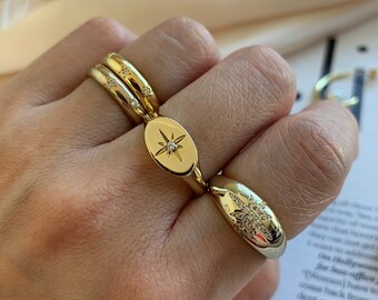 May include: Gold-toned ring set featuring a starburst design. The ring has an oval centerpiece with a starburst and a smaller ring with embedded crystals. The ring is worn on a finger.
