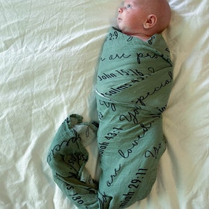 May include: A baby swaddled in a green muslin blanket with black text. The text includes bible verses and the words "You are loved."
