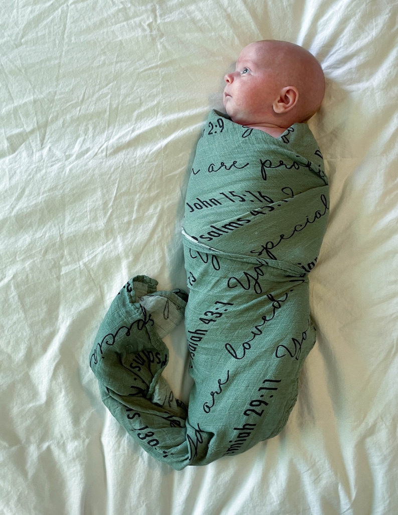 May include: A baby swaddled in a green muslin blanket with black text. The text includes bible verses and the words "You are loved."