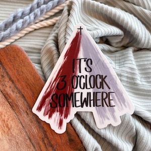 May include: A white sticker with a red and purple triangle design. The sticker has a cross at the top and the text "It's 3 o'clock somewhere".