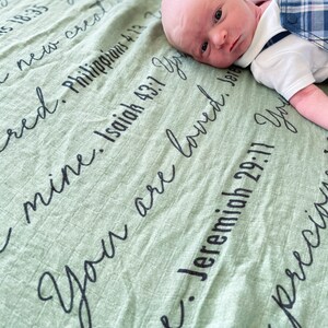 May include: A baby boy lying on a green blanket with the text "You are loved" and several bible verses written on it.