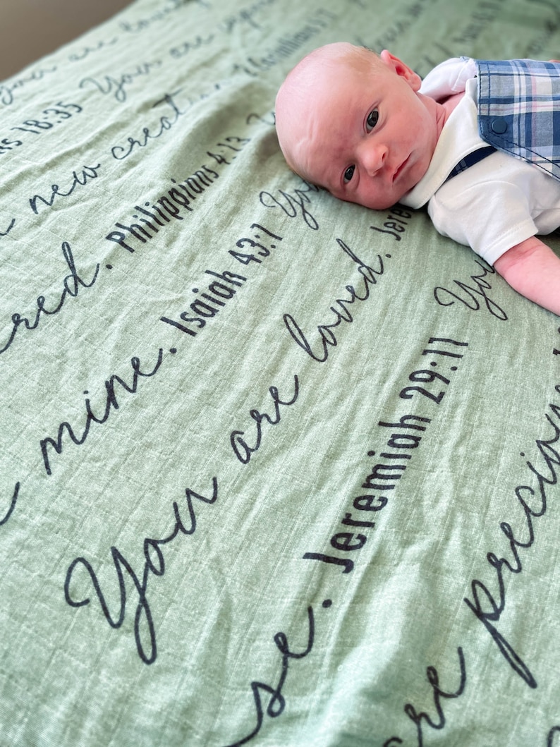 May include: A baby boy lying on a green blanket with the text "You are loved" and several bible verses written on it.