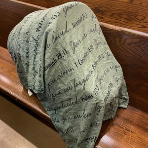 May include: A green throw blanket with black text printed on it. The text includes bible verses and phrases like "You are loved", "You are precious", and "You are family".