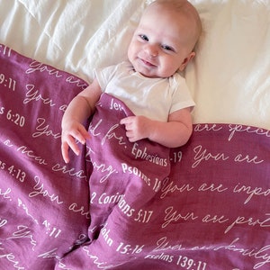 May include: A baby girl is lying on a pink and white blanket with white text that includes bible verses. The text reads "You are a new creation", "You are special", "You are important", "You are precious", "You are loved", and more.