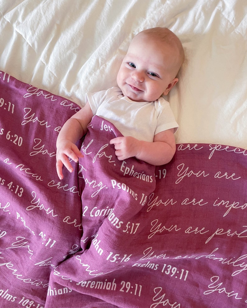 May include: A baby girl is lying on a pink and white blanket with white text that includes bible verses. The text reads "You are a new creation", "You are special", "You are important", "You are precious", "You are loved", and more.