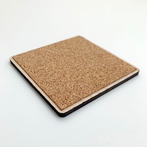 May include: A square coaster featuring a light brown, textured cork top surface layered over a dark brown wooden base. The coaster has clean, straight edges and a flat profile, showcasing the natural granular texture of the cork material.