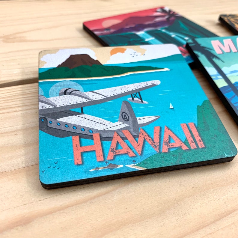 May include: A square coaster featuring a vintage-style illustration of a seaplane flying over a tropical island landscape with blue water, a dark mountain, and a small sailboat. The word HAWAII is printed in large, textured, coral-colored letters.