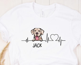 Puede incluir: Camiseta blanca con un gráfico de un perro asomándose sobre una línea de latido del corazón con un corazón y el nombre "JACK" debajo.