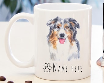 May include: White ceramic mug with a watercolor illustration of an Australian Shepherd dog. The dog has blue merle fur, brown eyes, and a pink tongue. The text "NAME HERE" is printed below the dog.