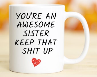 May include: White ceramic coffee mug with black text that reads "You're an awesome sister keep that shit up" and a red heart.