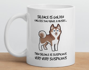 Puede incluir: Taza de café de cerámica blanca con una ilustración de un perro husky marrón y blanco. La taza tiene texto negro que dice "Silence is golden unless you have a husky... Then silence is suspicious very very suspicious."