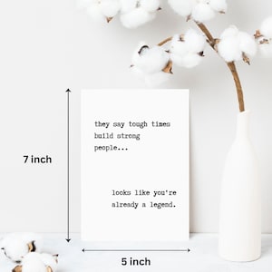May include: A white card with black text that reads "they say tough times build strong people... looks like you're already a legend." The card is 17.8 cm tall and 12.7 cm wide.