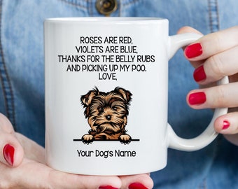 May include: White ceramic coffee mug with a Yorkshire Terrier peeking over the rim. The mug has a humorous message that reads "Roses are red, violets are blue, thanks for the belly rubs and picking up my poo. Love, Your Dog's Name."
