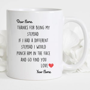 May include: White ceramic coffee mug with black text that reads "Dear Name, THANKS FOR BEING MY STEPDAD IF I HAD A DIFFERENT STEPDAD I WOULD PUNCH HIM IN THE FACE AND GO FIND YOU LOVE Your Name" with a red heart.