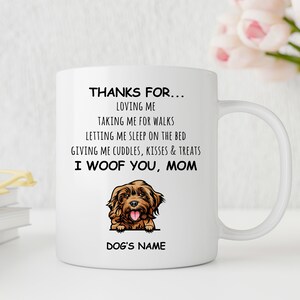 Puede incluir: Taza de café de cerámica blanca con una ilustración de un perro marrón y el texto "THANKS FOR... LOVING ME TAKING ME FOR WALKS LETTING ME SLEEP ON THE BED GIVING ME CUDDLES, KISSES & TREATS I WOOF YOU, MOM DOG'S NAME"