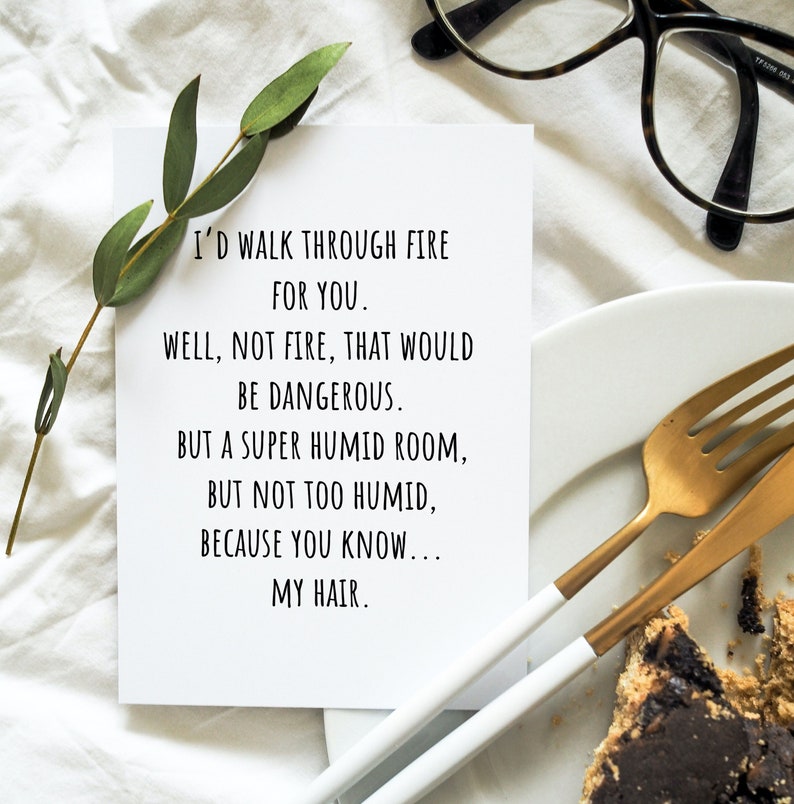 May include: A white card with black text that reads, "I'D WALK THROUGH FIRE FOR YOU. WELL, NOT FIRE, THAT WOULD BE DANGEROUS. BUT A SUPER HUMID ROOM, BUT NOT TOO HUMID, BECAUSE YOU KNOW... MY HAIR." The card is next to a sprig of greenery, a plate, and gold silverware.