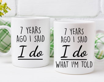 May include: Two white coffee mugs with black text. The mug on the left says "7 years ago I said I do". The mug on the right says "7 years ago I said I do what I'm told".
