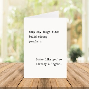 May include: A white card with black text that reads "they say tough times build strong people... looks like you're already a legend."