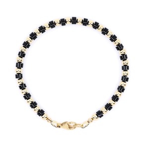 May include: A circular bracelet featuring an alternating pattern of small, polished black cylindrical beads and smooth, reflective gold-toned spherical beads. The piece is secured with a gold-toned lobster claw clasp at the bottom center.