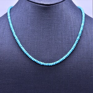 May include: A turquoise beaded necklace on a gray mannequin. The necklace is made of small, round beads that are strung together on a silver chain.