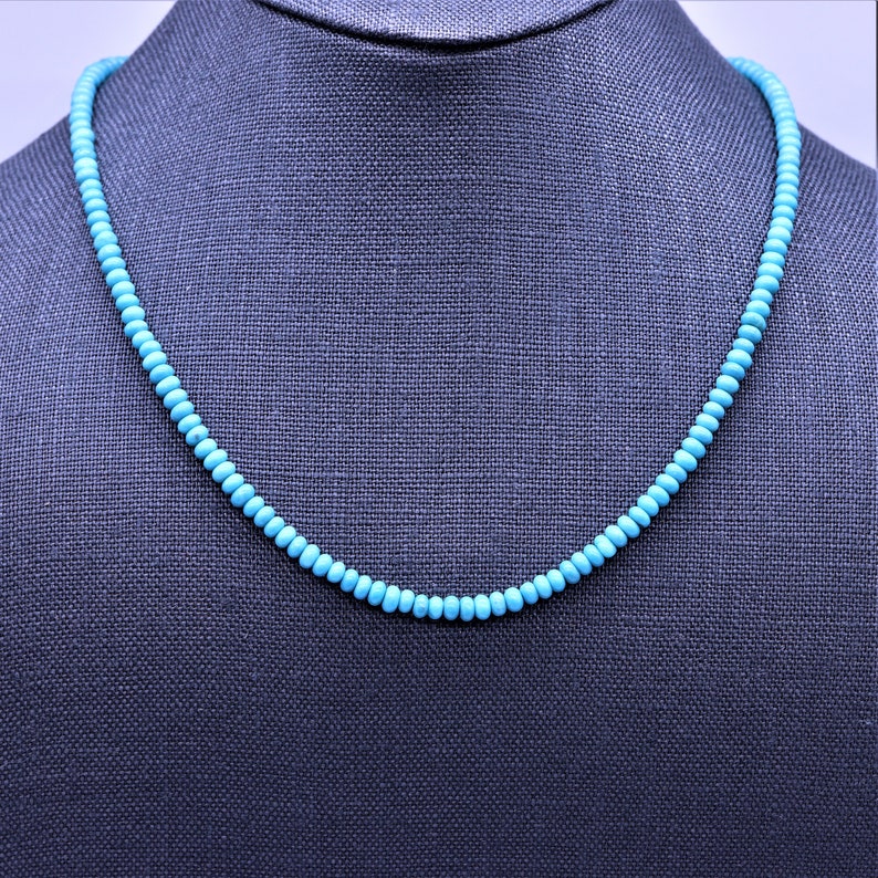 May include: A turquoise beaded necklace on a gray mannequin. The necklace is made of small, round beads that are strung together on a silver chain.