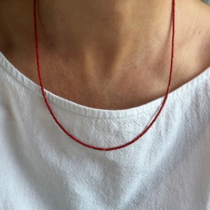 May include: A red beaded necklace made of small, round beads. The necklace is worn by a person, but the person's face is not visible.