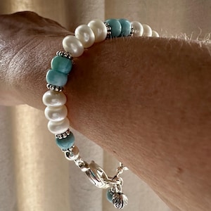 May include: A bracelet with white pearls and blue-green stones. The bracelet has a silver clasp and a silver charm.