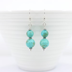 May include: A pair of silver dangle earrings with two turquoise beads on each earring.