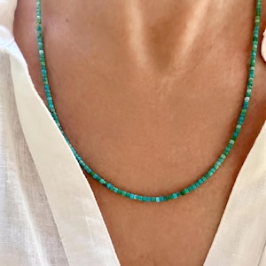 May include: A delicate necklace composed of small, square-shaped beads in varying shades of turquoise, teal, and seafoam green. The beads are strung together in a continuous, uniform strand that rests against the collarbone area.