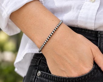 May include: A delicate bracelet composed of a single strand of small, polished, metallic silver-toned spherical beads. The beads are uniform in size and shape, creating a continuous, smooth, and reflective circular line around the wrist.