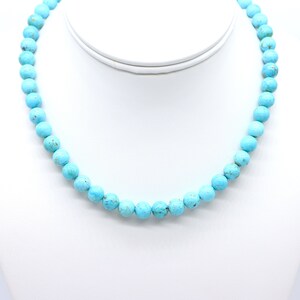May include: A turquoise beaded necklace with round beads. The necklace is on a white mannequin bust.