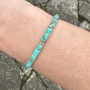 May include: A turquoise and gold beaded bracelet. The bracelet is made of small, round beads that are strung together on a thin cord. The beads are a light turquoise color with a slight green hue, and they are interspersed with small, gold beads.