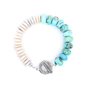 May include: A bracelet featuring a half-strand of smooth, cream-colored disc beads and a half-strand of round, mottled turquoise beads. The two sections are connected by a silver-toned metal toggle clasp with a textured, radial line pattern.