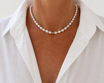 May include: A necklace composed of white, slightly irregular, teardrop-shaped pearls strung together. The necklace features a small, central gold-toned metal bead spacer that connects the pearls at the front, resting against the base of the neck.