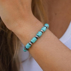 May include: A turquoise beaded bracelet with silver-colored spacers. The bracelet is worn on a wrist, with the skin tone visible. The beads are a vibrant blue-green color, and the spacers are round and metallic.