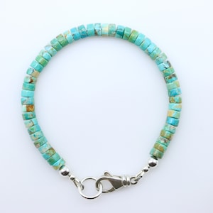 May include: A turquoise gemstone bracelet with a silver clasp. The bracelet is made of square-shaped beads.