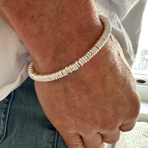 May include: A silver-toned bracelet composed of numerous small, rounded, disc-shaped beads strung together in a continuous circular formation. The metallic surface of the beads reflects light, creating a bright, polished appearance around the wrist.