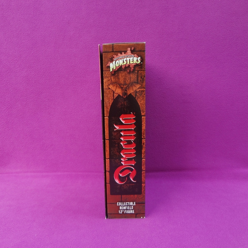 May include: A collectible 12-inch figure box featuring the Universal Studios Monsters logo and the name "Dracula" in red script. The box has a brick-like design with a bat graphic.