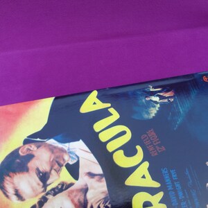 May include: A vintage movie poster for "Dracula" with a purple background. The poster features a portrait of a man and the title in large yellow letters. Additional text includes names and the phrase "12" figure."