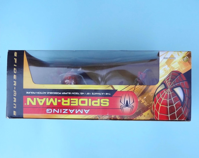 Puede incluir: Una figura de acci&oacute;n de Spider-Man en una caja. La caja es roja, amarilla y negra, con las palabras "Spider-Man" y "Amazing" en un lugar destacado. La figura es visible a trav&eacute;s de una ventana de pl&aacute;stico transparente. La caja mide 45,72 cm.
