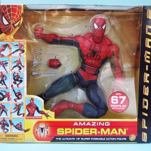 Puede incluir: Figura de acci&oacute;n de Amazing Spider-Man en un embalaje de pl&aacute;stico transparente. La figura es roja y negra con un emblema de ara&ntilde;a en el pecho. El embalaje incluye el texto "Amazing Spider-Man" y "La figura de acci&oacute;n s&uacute;per posable de 45.7 cm."