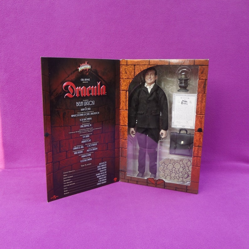 May include: A Dracula Bela Lugosi action figure in a display box. The figure wears a black coat, white shirt, and purple pants. Accessories include a briefcase, lantern, and a document. The box features the movie title and cast list.