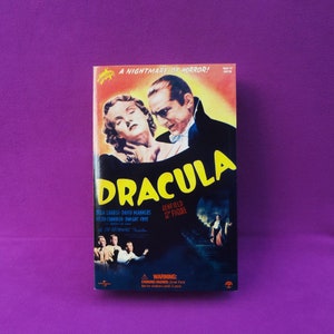 May include: A vintage Dracula movie poster-style box featuring Bela Lugosi. The box art includes the movie title in yellow, cast names, and the phrase "A Nightmare of Horror!". The figure is labeled as a 12" figure.