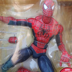Puede incluir: Figura de acci&oacute;n de Spider-Man en un embalaje de pl&aacute;stico transparente. La figura es predominantemente roja y azul, con un emblema de ara&ntilde;a negra en el pecho. Presenta patrones de telara&ntilde;a detallados y accesorios.