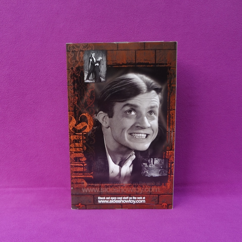 May include: A rectangular product box featuring a black and white image of a man with a wide grin, looking upwards. The box has a brick-like border with additional small images and text, including the website address www.sideshowtoy.com.