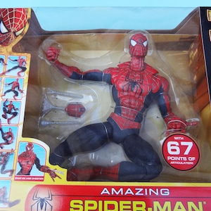 Puede incluir: Figura de acci&oacute;n de Amazing Spider-Man en una vitrina de pl&aacute;stico transparente. La figura es roja y negra con un emblema de ara&ntilde;a en el pecho. El embalaje incluye el texto "WITH 67 POINTS OF ARTICULATION!"