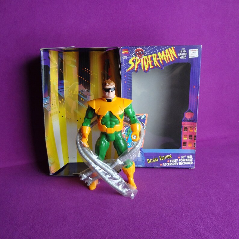 May include: A green and yellow action figure of Doctor Octopus from the Spider-Man animated series. The figure is holding its four tentacles and is posed in a fighting stance. The figure is packaged in a box with the Spider-Man logo and the words "Deluxe Edition".