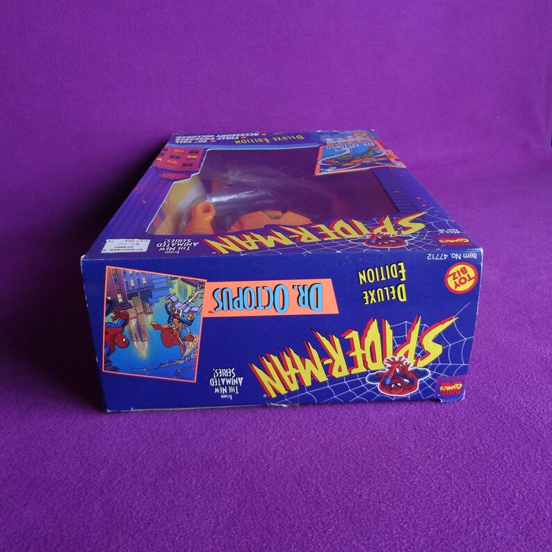 May include: A blue and yellow box with a Spider-Man action figure inside. The box features a cartoon image of Spider-Man and Dr. Octopus. The text on the box reads "Spider-Man Deluxe Edition Dr. Octopus".